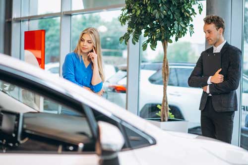 Mulher loira numa loja de carros junto ao vendedor pensando em comprar um carro.